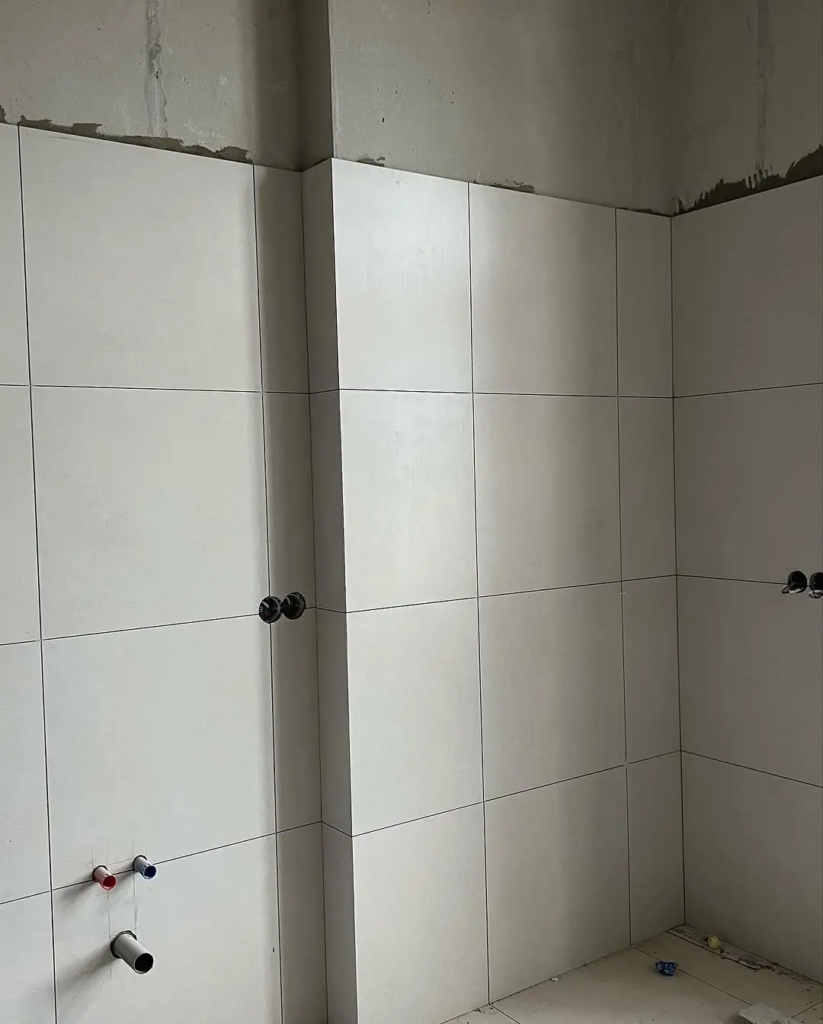 Detailná realizácia obkladu steny veľkoformátovou svetlosivou dlažbou v kúpeľni