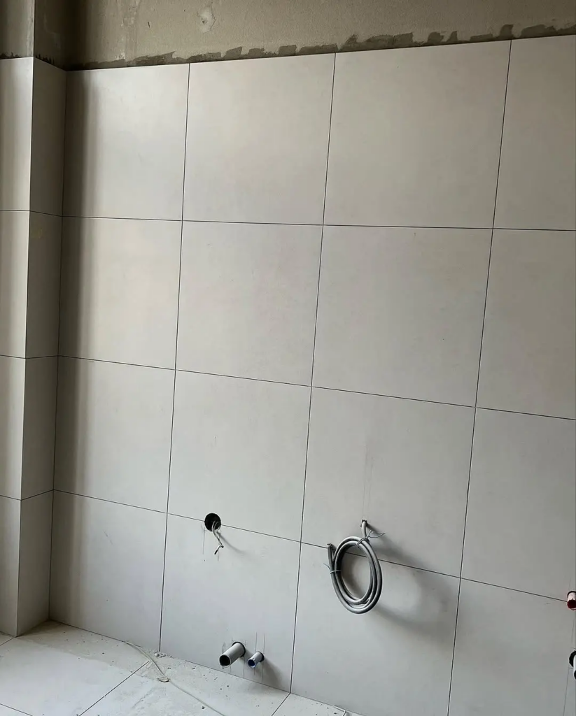 Detailná realizácia obkladu steny veľkoformátovou svetlosivou dlažbou s výrezmi pre inštalácie